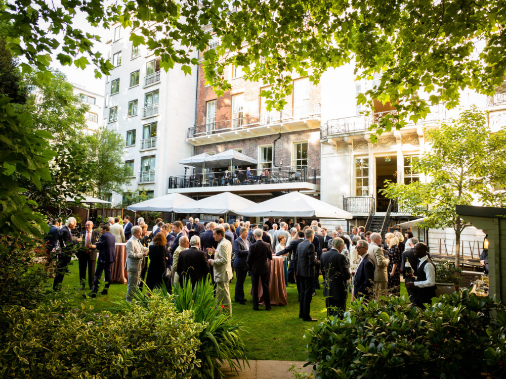 an outdoor garden party at the Royal Overseas league - all the guests in black suit