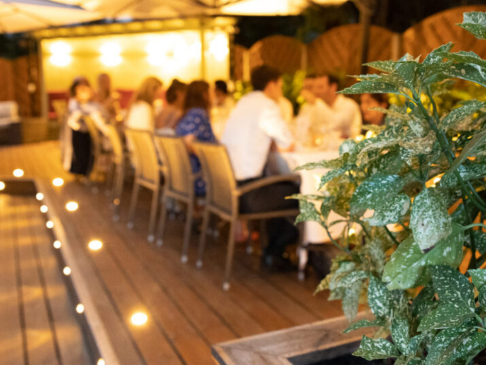Guests sitting outside at night on a wooden deck with bright background lighting