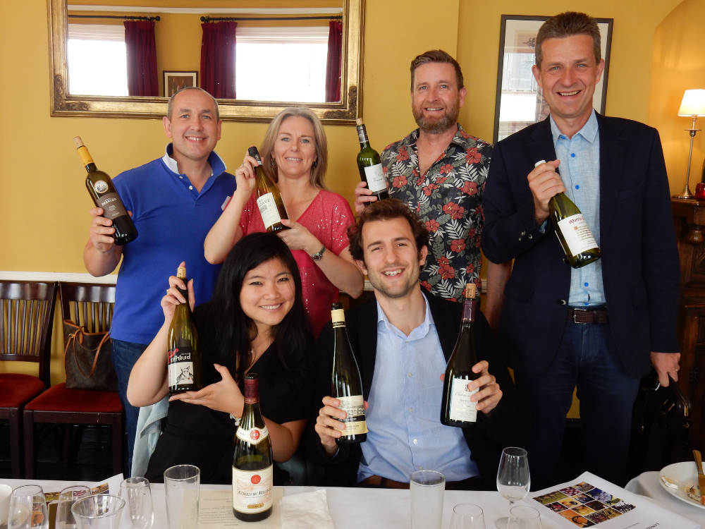 A group of six guests showing their favourite wines to the camera