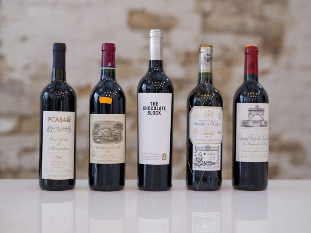 five individual red wines standing in a row on a white table
